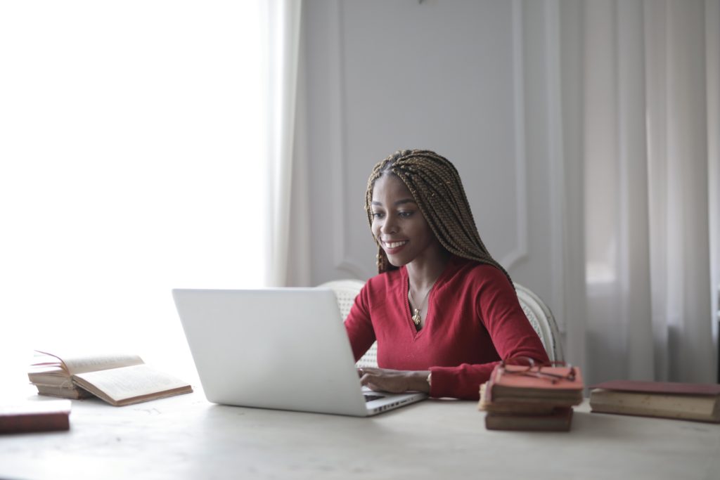 A young woman smiles while working on a laptop