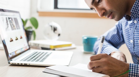 Young man working on a computer and taking notes