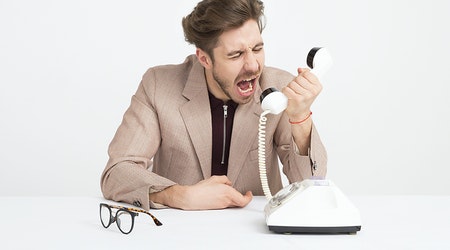 Man in a suit angrily yelling into the telephone