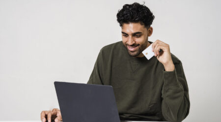 A man sits in front of his laptop holding a credit card