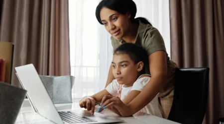 A woman and her child look at a laptop at a desk